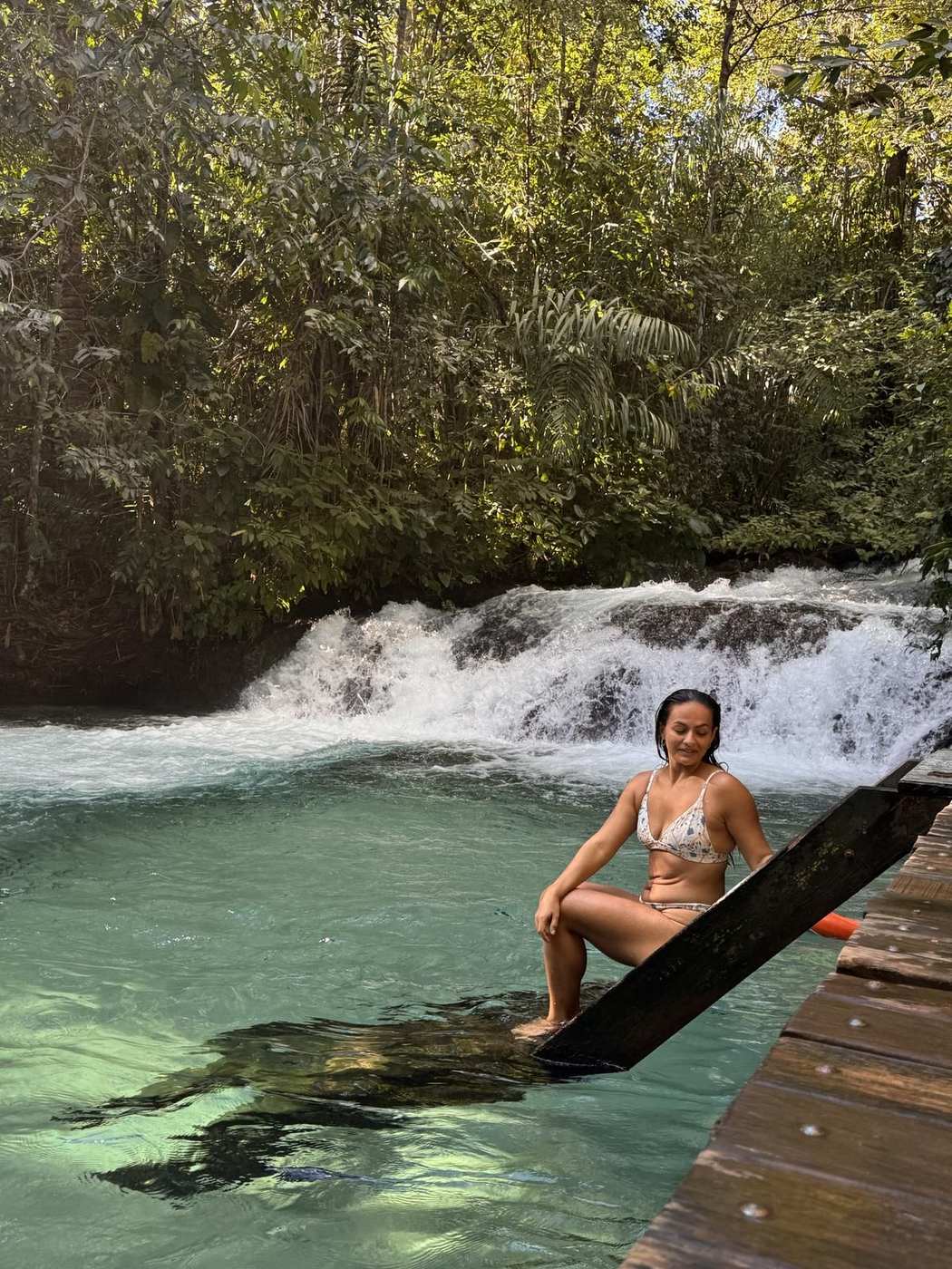 Isadora sentada na plataforma da Cachoeira da Formiga, água azul-turquesa