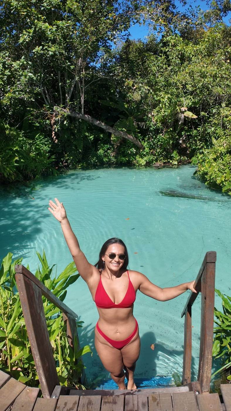 Isadora acenando na escada de um fervedouro de água azul