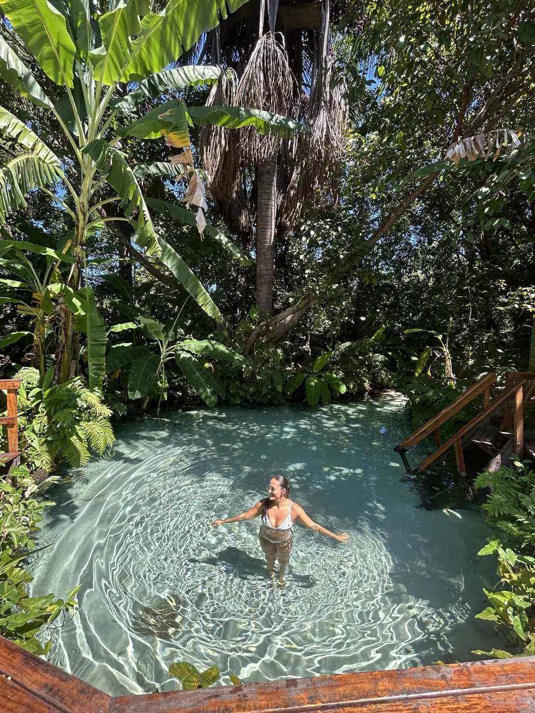 Isadora boiando num fervedouro de água azul cercado de mata