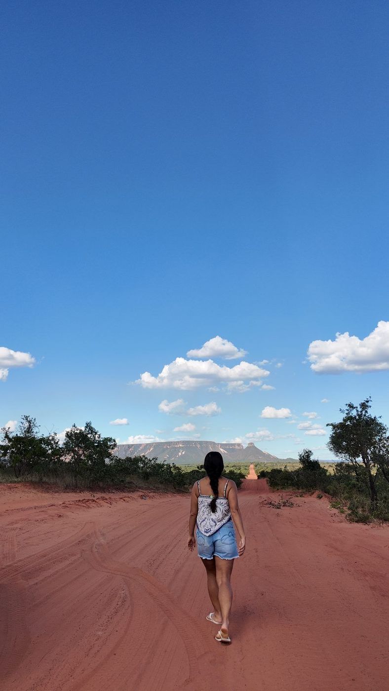 Isadora caminhando numa estrada de terra vermelha sob céu azul